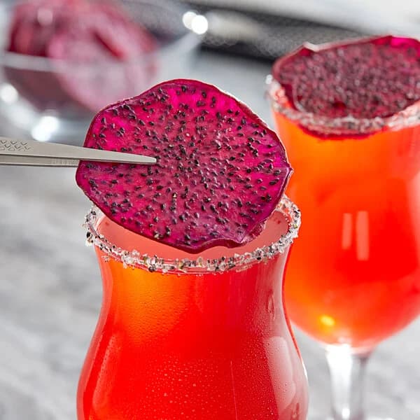 Tweezers placing a dried dragon fruit slice on a salt-rimmed glass of red cocktail.