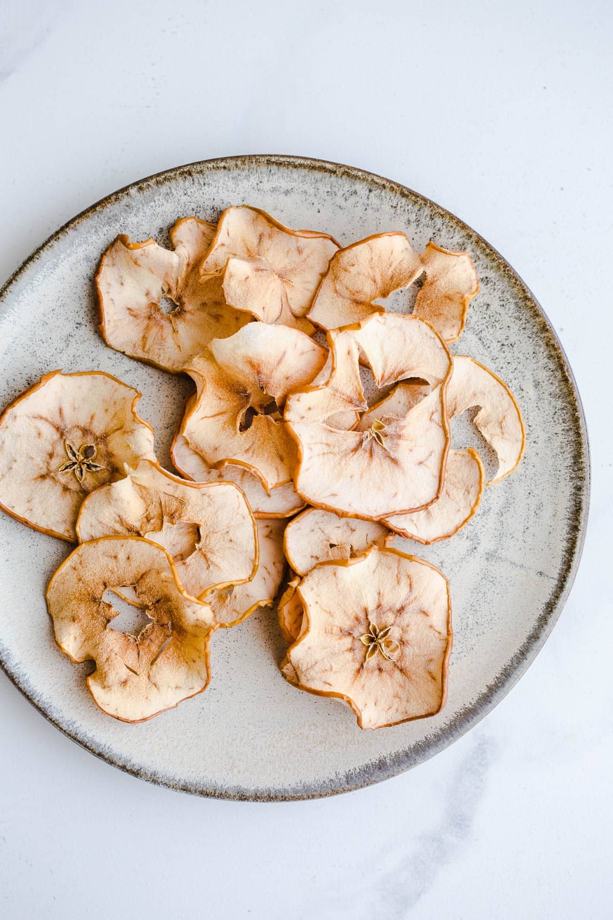Wavy, thin dried apple slices with visible core patterns on a speckled ceramic plate.