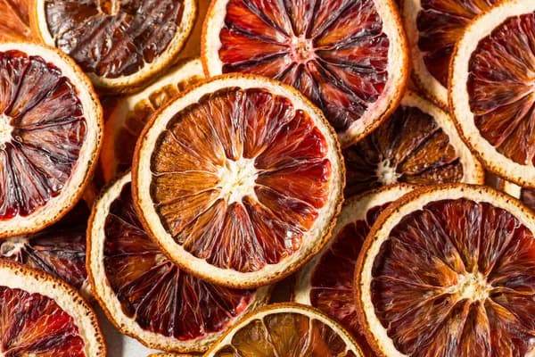 Overlapping slices of dried blood orange with deep red pulp and thin, light-colored rinds.
