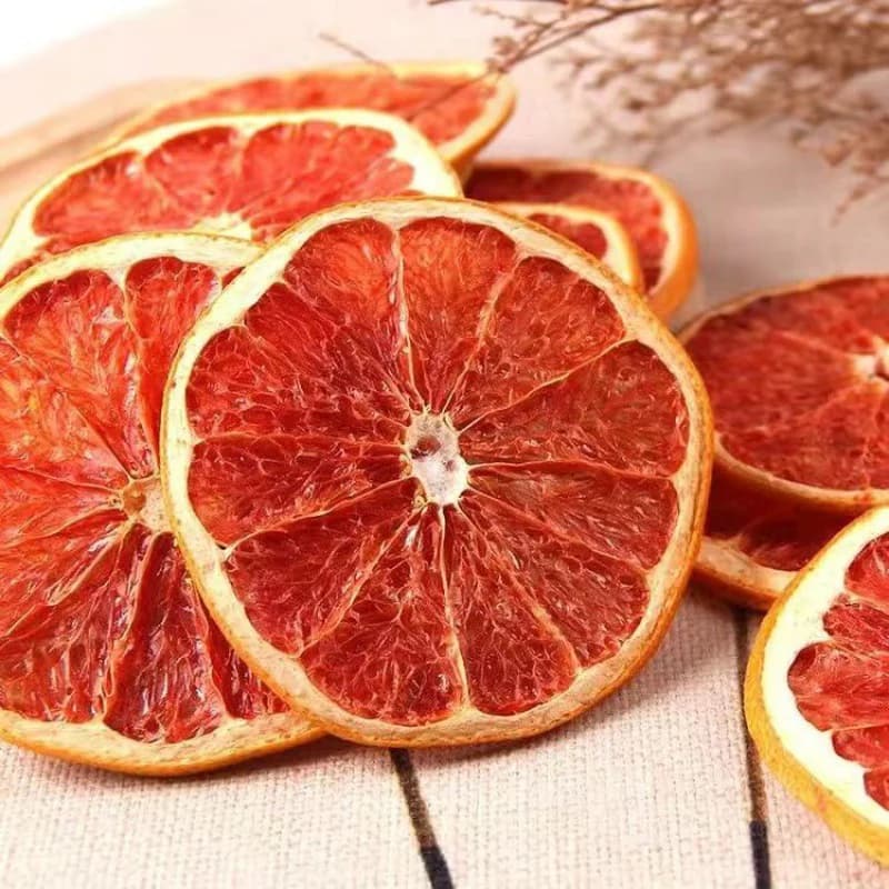 Vibrant red dried grapefruit slices with thin rinds arranged on a light textured surface.